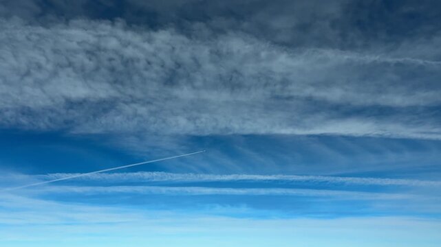 A Jet Cockpit view flying. at high-altitude with the view of multiple dissipating parallel contrais under a deep blue sky, with a jet crossing in diagonal left to right.