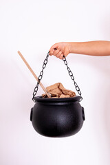Hand holding black cauldron with wooden spoon and brown paper against white background