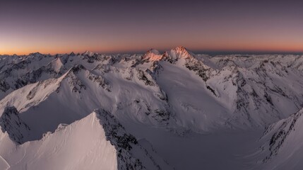 Majestic snow-covered mountain peaks under a soft pink and twilight blue sky during sunrise or sunset,