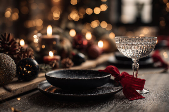 Cozy festive holiday table with candlelight bokeh, crystal glassware, black plates and red ribbon — rustic Christmas ambience - Powered by Adobe