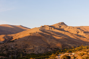 Naklejka premium Golden hour light on arid mountain landscape with clear sky.