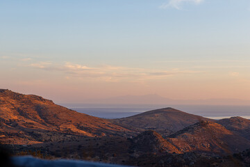 Serene landscape of rolling hills with a distant view of the sea at sunset.