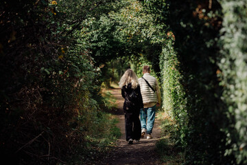 Fototapeta premium Young Couple Walking Hand in Hand Through a Green Tunnel, Back View Only