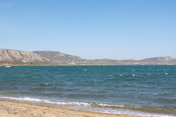 A serene coastal landscape with a calm sea and distant hills under a clear blue sky.