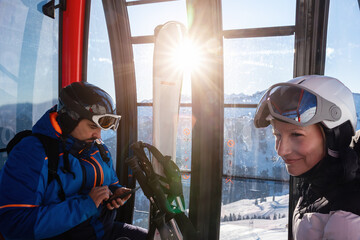 Scenic two skiers study trail map inside ski lift gondola at warm sunrise light at mountain alpine resort. Scenery group friends teamwork, planning, and excitement downhill winter sports adventure