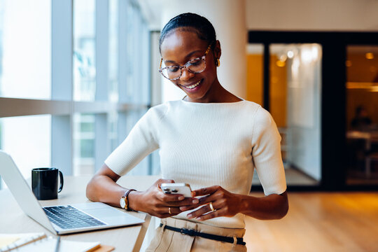 Professional woman using a smartphone at desk with a laptop