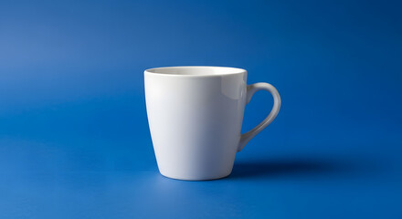 Obraz premium A simple white ceramic mug with a handle isolated against a solid blue background in studio light