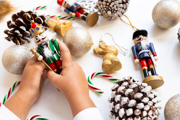 Child hands holding nutcracker among festive Christmas ornaments and pinecones