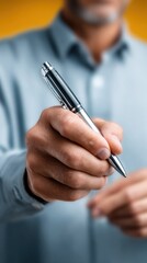 Man Holds Pen Ready To Write On Yellow Background With Soft Lighting