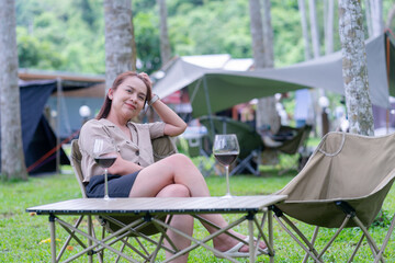 Smiling Woman Enjoying Red Wine and Leisurely Glamping Vacation, Portrait of a Happy Adult Female Relaxing at a Campsite in Nature, Peaceful Getaway: Middle-Aged Woman Sitting by Wine Glasses Outdoors