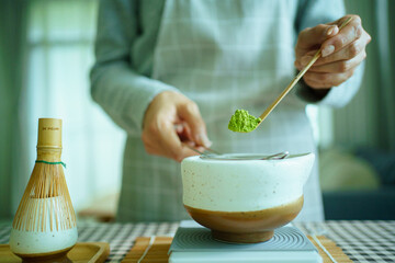 Woman sifting matcha powder into bowl on digital scale.