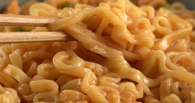 Korean spicy ramyeon noodle soup, with spices and green onions. Chopsticks pick up noodles.