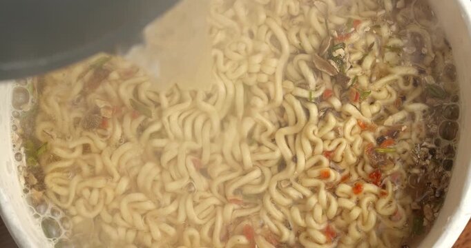 Instant noodles with spices are poured with boiling water, top view.