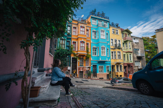 Istanbul, Turkiye - 06 October 2019: View of a woman sitting on steps amidst the vibrant, colorful facades of buildings in Balat, a historic district.