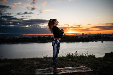 Fototapeta premium Yoga instructor practicing at sunset by the river