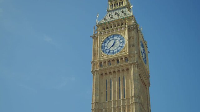Tilt shot of the Elizabeth Tower with the Big Ben clock face under a bright blue sky on a sunny day in London, England. Close up shot of Big Ben clock tower with clear sky in the background.