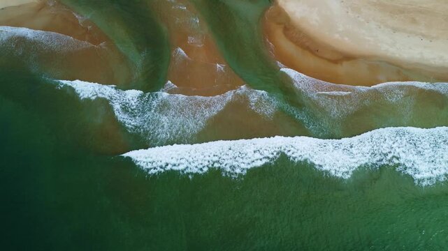 Aerial view of ocean waves breaking on a sandy beach with river water mixing in