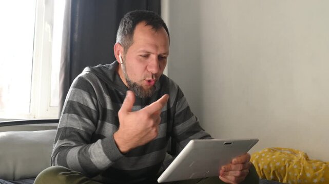 bearded man with wireless headphones communicates via video call over internet. Emotional gestures and smile. Long-distance friendship. He's video chatting with girl. Romance and love without barriers