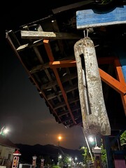 Traditional bamboo kentongan hanging under a wooden structure at night, illuminated by streetlights and moonlight.