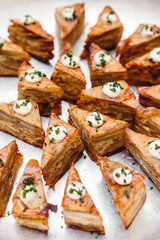 Close-up of elegant gourmet appetizers made of layered potatoes or savory cake, topped with cream and chopped chives, arranged on a silver serving tray. Perfect for catering, gastronomy.