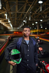 Young racer stands proudly ready for an exciting karting adventure indoors