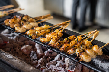 Grilled skewers of marinated shrimp cooking over hot coals in a street food setting during a sunny afternoon