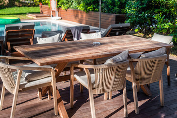 Outdoor dining area with wooden table and chairs near swimming pool on a sunny day
