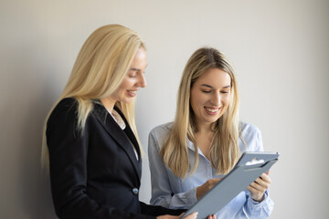 Two focused blonde businesswomen collaborate in an office, using a caliper to measure something on...