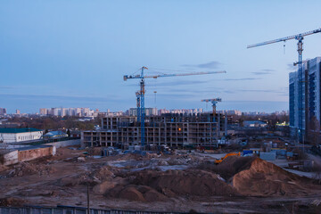 Construction site with cranes and unfinished buildings at dusk in city