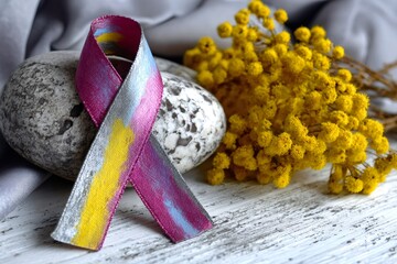 Bladder cancer awareness ribbon resting on stone with yellow flowers