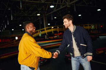 Friends enjoying leisure time at a go karting venue while sharing a joyful handshake