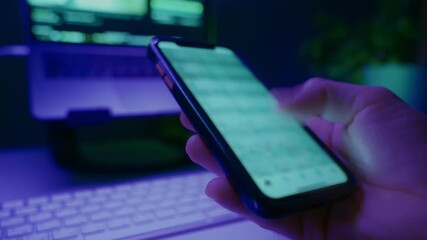 Hand holding smartphone and quickly scrolling social media feed in dark room with desk on background, illuminated by blue and purple neon light. Digital addiction and mindless content consuming - Powered by Adobe