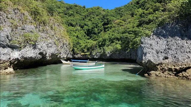 Small boats float in a tranquil turquoise cove surrounded by lush, rocky cliffs