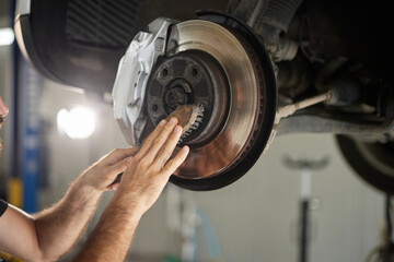 A technician inspects and cleans the brake rotor of a vehicle in an auto repair shop. The workspace is organized, with tools and equipment nearby.