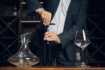 Sommelier opening wine bottle with corkscrew in elegant restaurant setting. Concept of hospitality and service excellence showing emotional focus and ritual precision.