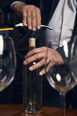 Sommelier opening white wine bottle with steady hands and focus. Concept of professional craftsmanship and patience symbolizing hospitality and mindfulness.