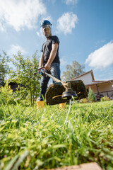 A man in a protective mask with a trimmer mows grass - wide-angle lens view from below