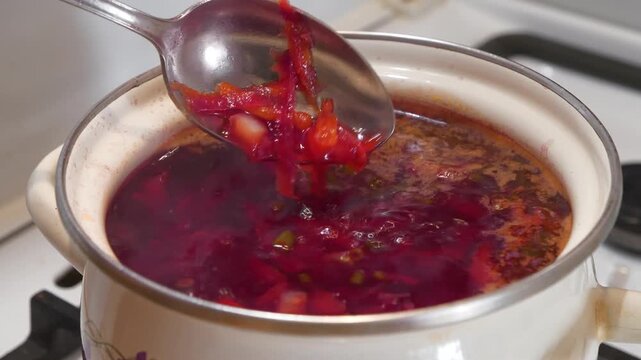 Ukrainian borscht is cooked on stove. Cook stirs borscht with spoon. National dish of Ukraine. Main first course of Ukrainian cuisine. Cooking first courses.Red Ukrainian borsch is boiling in saucepan