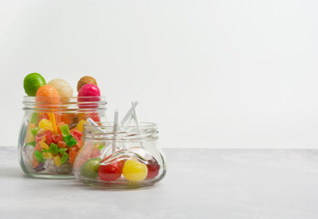Multicolored and assorted lollipops are in glass jars on a gray background. View straight ahead