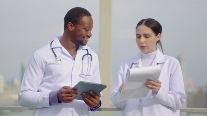 Latin female doctor talking with African American male colleague during work break rooftop of the hospital. Friendly conversation between two doctors during a lunch break of a clinic