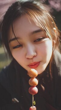 A close-up of A Japanese teenage girl holding a dango skewer under cherry blossoms in a Tokyo park
