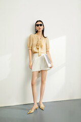 Stylish woman in a trendy outfit holding a notebook, standing in a bright studio.