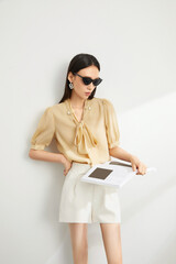 Woman in a yellow blouse and white skirt poses confidently against a minimal background.