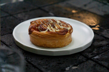 A savory ham and cheese roll with a golden, flaky crust is served on a white plate, set against a dark, moody background with reflective water droplets.