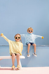 Two children wearing colorful shirts and sunglasses, playing outdoors with joy.