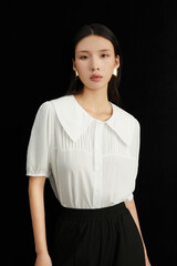Woman in a white blouse with a collar posing elegantly against a black background.