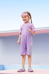 Joyful girl in a purple swimsuit smiling outdoors by the pool.