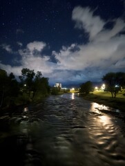 A serene night river reflects starlight and distant city lights with gentle moonlight illuminating the water s tranquil rippling surface under a