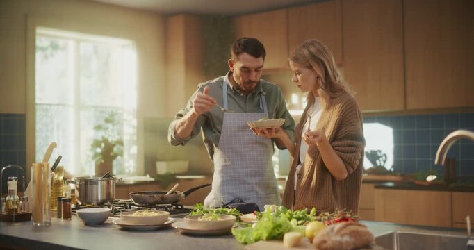 Happy Couple Standing Close Together in the Kitchen, Eating Pasta from a Shared Bowl. They Laugh and Compliment Each Other’s Cooking, Enjoying Their Homemade Italian Dish