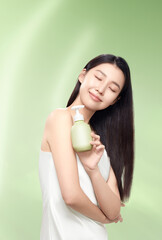 Woman holding green skincare bottle with a joyful expression in a serene setting.